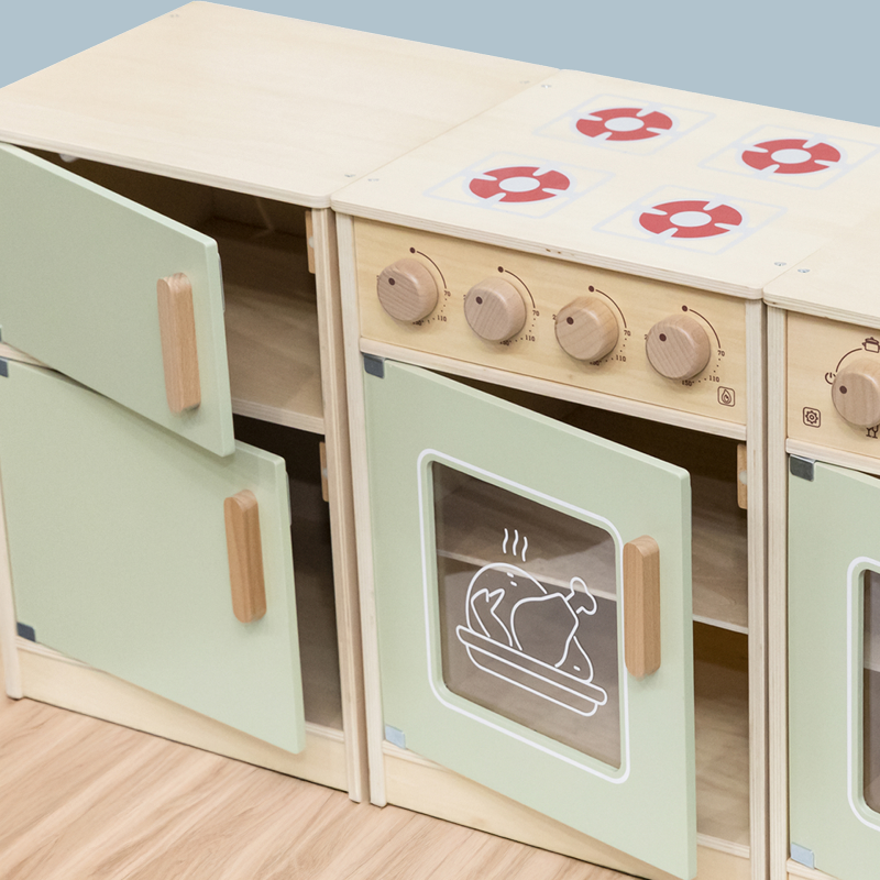 Wooden toy kitchen set with green cabinets and beige stove top on a light wooden floor.