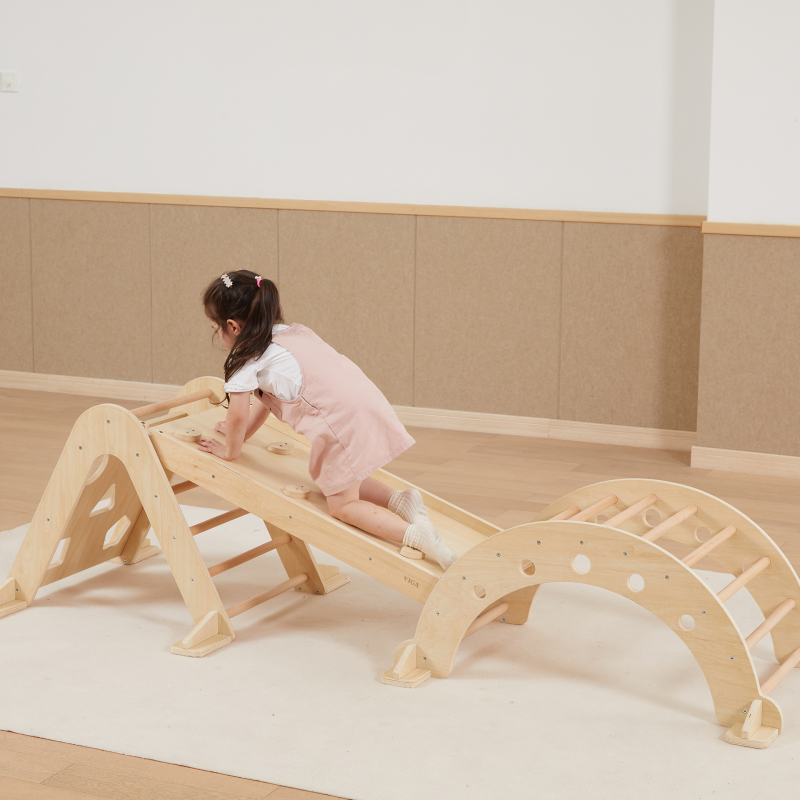Child playing on a wooden climbing toy in a room with beige walls and flooring.