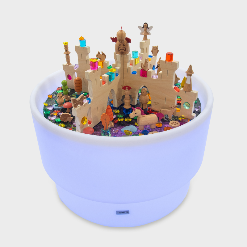 Toy castle set in a glowing purple sensory table with small castle figurines