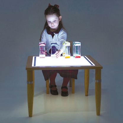 Child sitting at a light table with colourful objects on a dark background