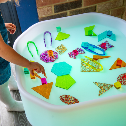 Children's play table with colorful geometric shapes and a child's hand reaching in.