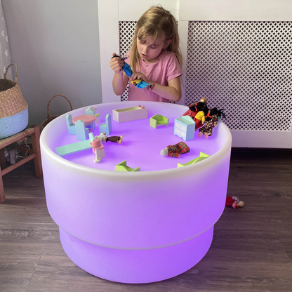 Child playing with toys on a colorful LED table in a room.