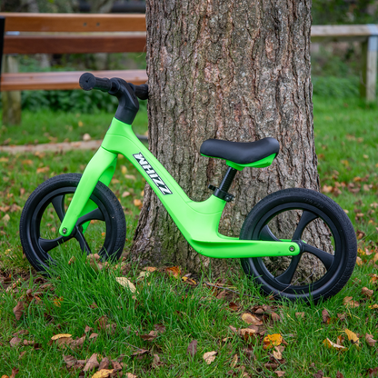 Green balance bike leaning against a tree in a park setting