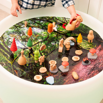 Wooden forest toy set on a round sensory light play table with a scenic background