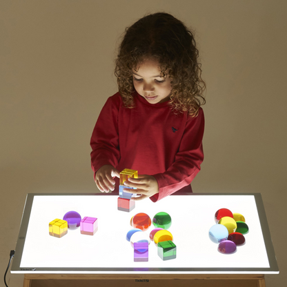 Child playing with colorful blocks on a light-up table against a plain background