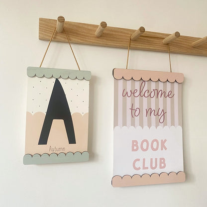 Two decorative signs hanging on a wooden rod against a white wall.