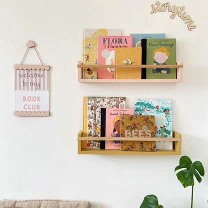 Wooden bookshelf with children's books on a white wall, featuring decorative signs.