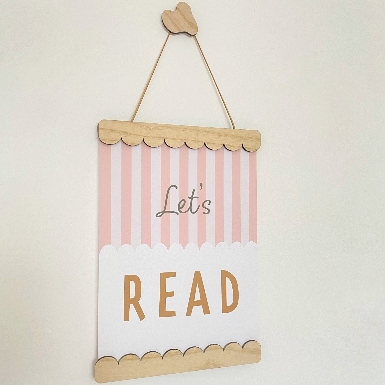 Decorative sign with 'Let's Read' text on a striped background, hanging against a light beige wall.
