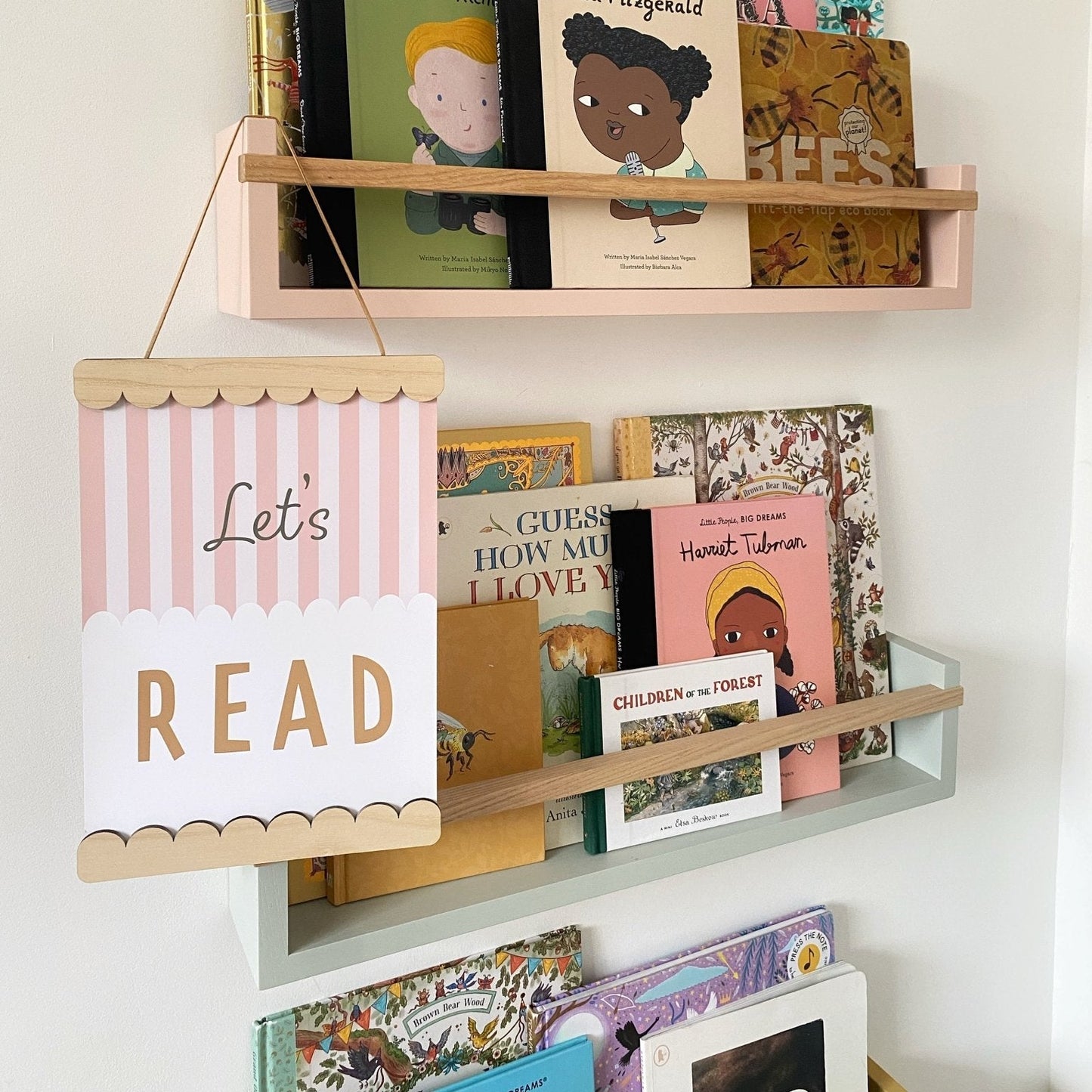 Children's books on a shelf with a 'Let's Read' sign against a white wall.