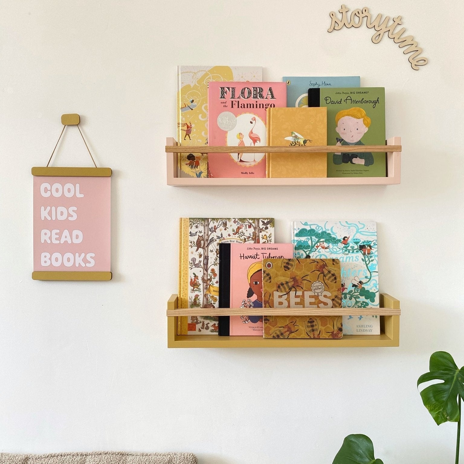 Wooden bookshelf with children's books on a wall, next to a pink sign and plant.
