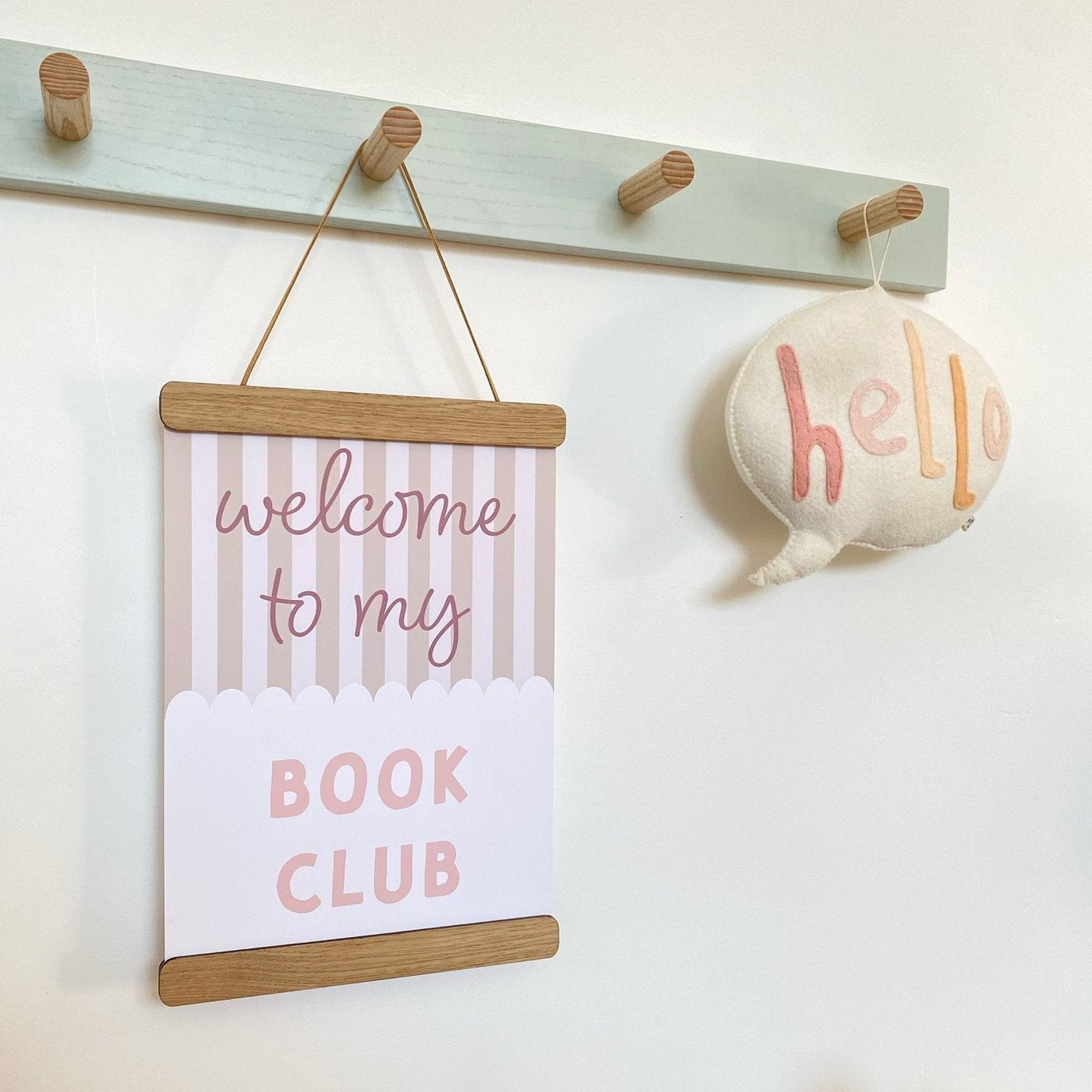 Decorative sign with 'welcome to my book club' text hanging on a wall with hooks and a plush toy.