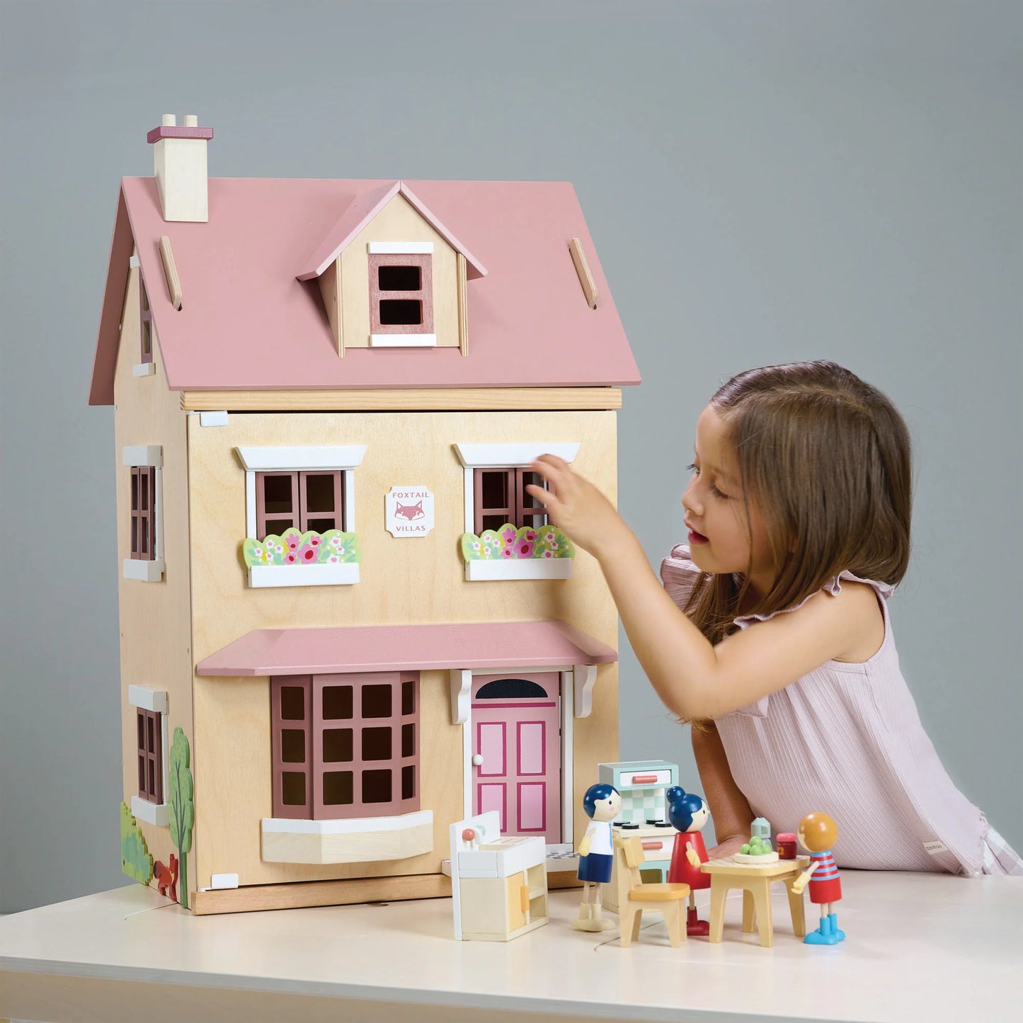 Child playing with a wooden dollhouse and accessories on a gray background