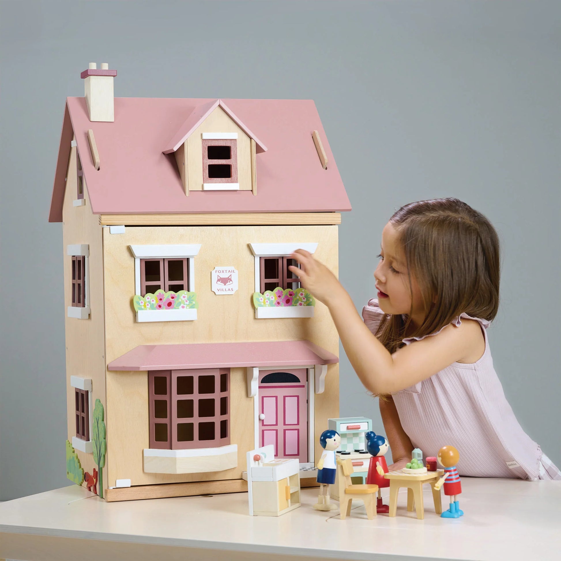 Child playing with a wooden dollhouse and accessories on a gray background