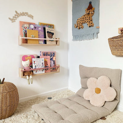Children's room with a beige floor pillow, wall hanging, and shelves.