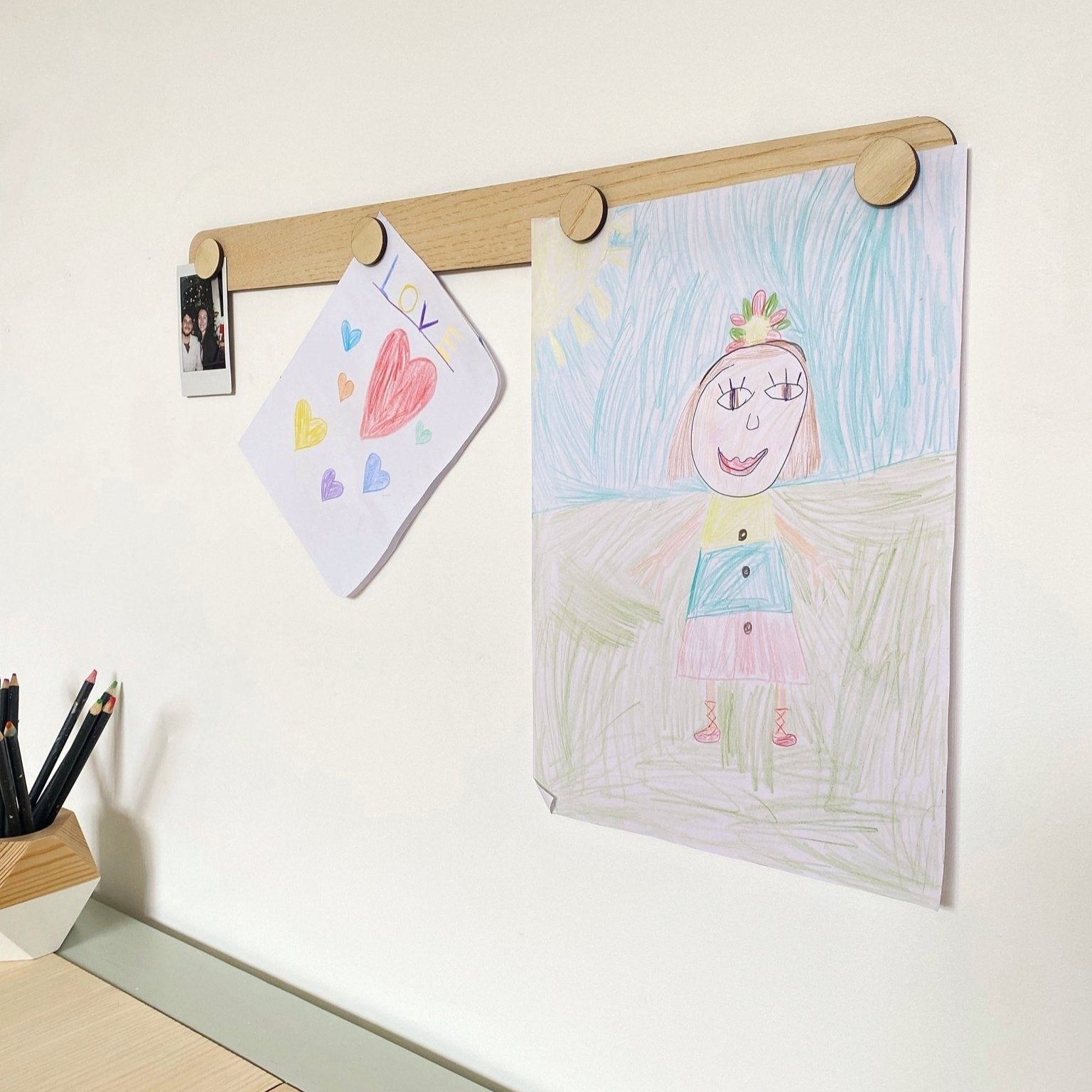 Children's drawings on a wooden frame against a white wall.