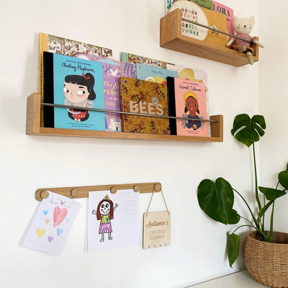Wooden shelves with children's books and drawings on a white wall.