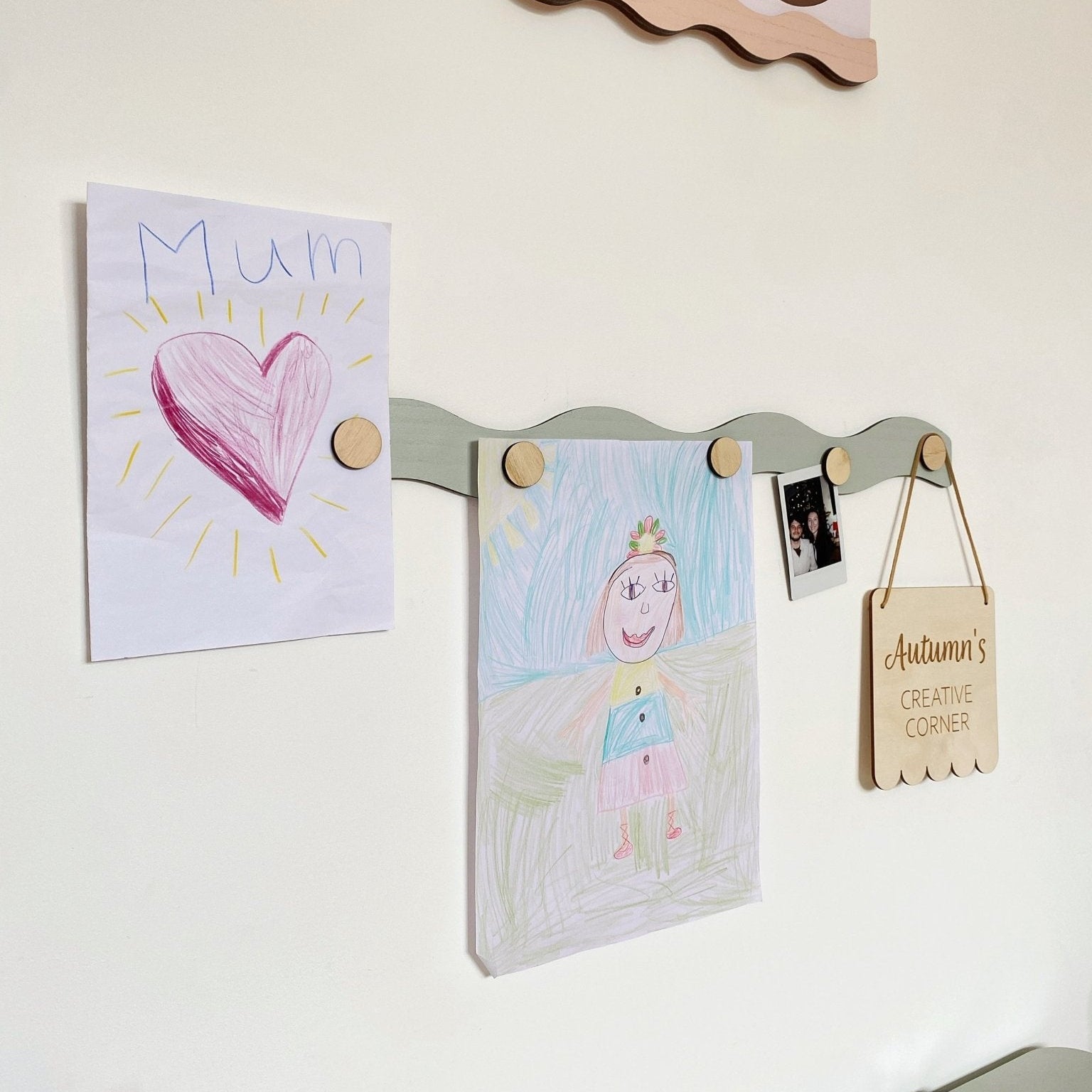 Children's artwork and notes displayed on a magnetic board with wooden pegs.