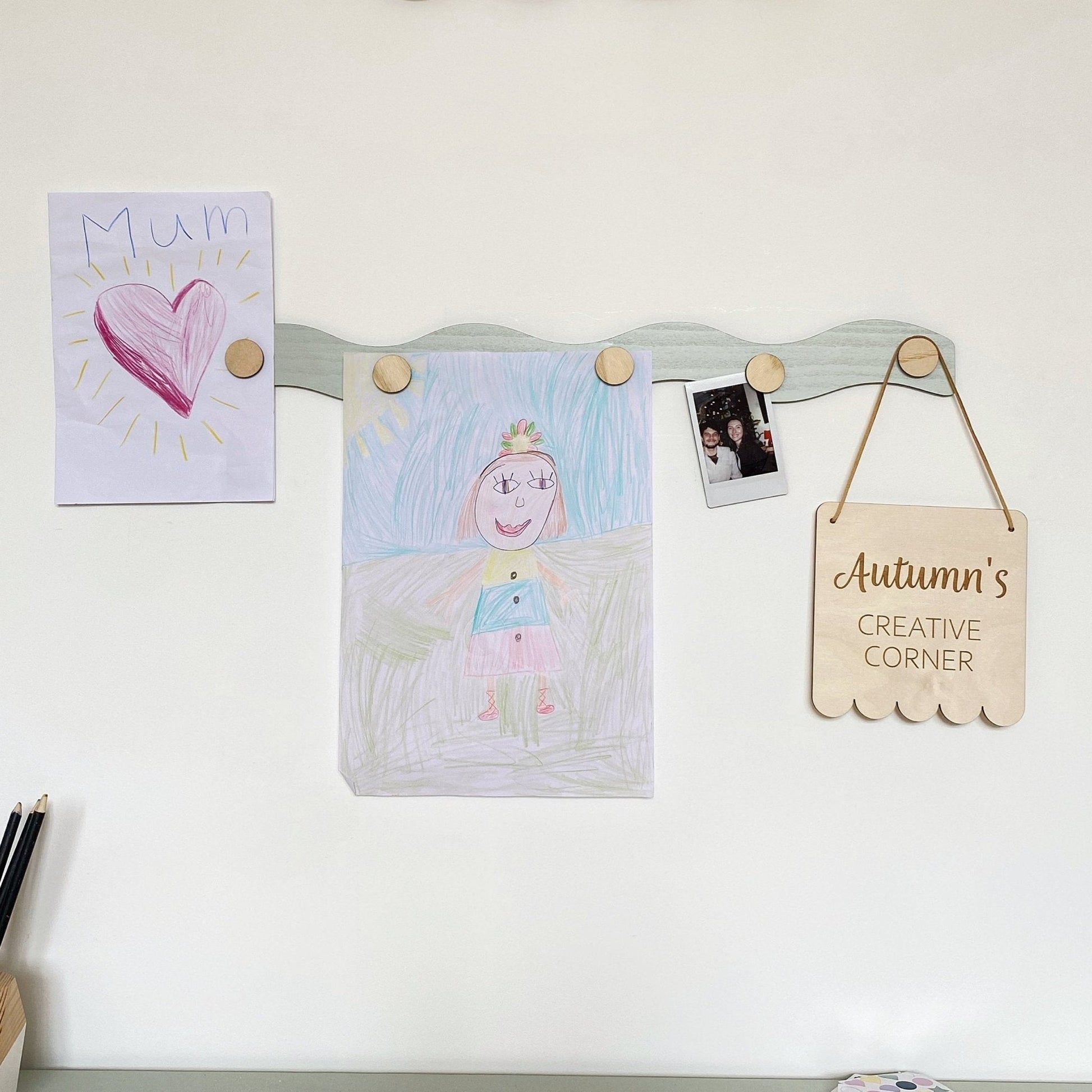 Children's artwork and a sign on a magnetic board against a white wall.