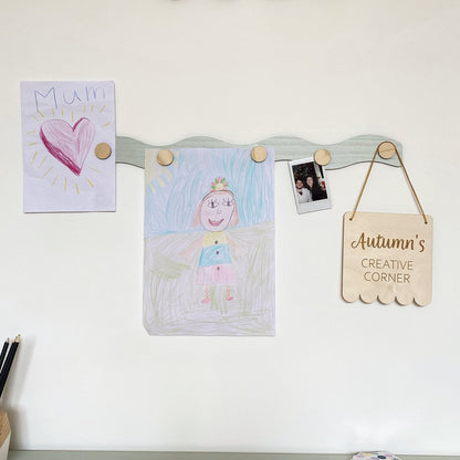 Children's artwork and a sign on a magnetic board against a white wall.