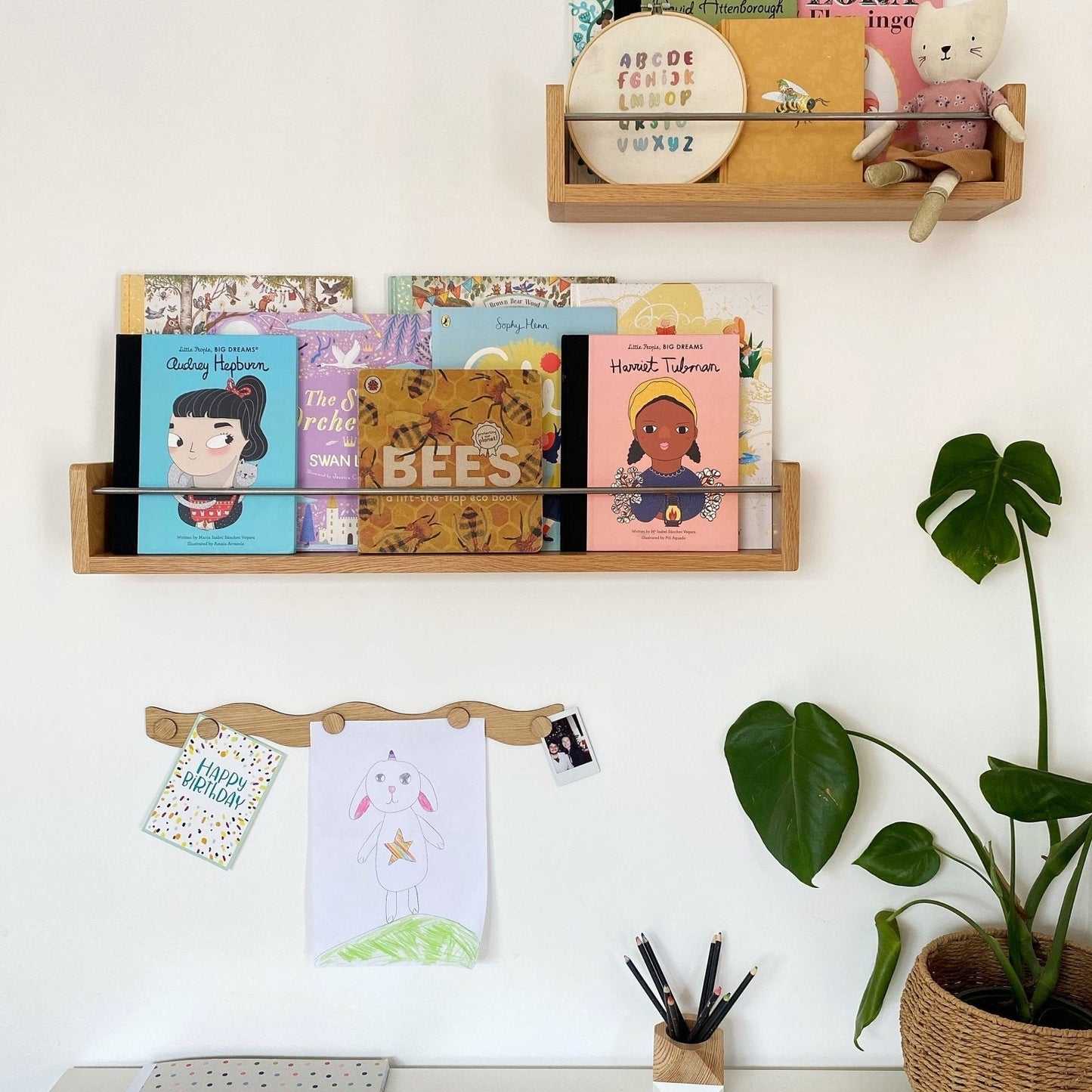 Wooden shelves with books and stationery on a white wall, next to a plant.