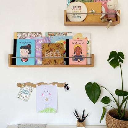 Wooden shelves with books and stationery on a white wall, next to a plant.
