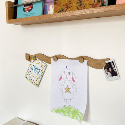 Wooden wall-mounted rack with children's drawings, cards, and a photo on a white wall.