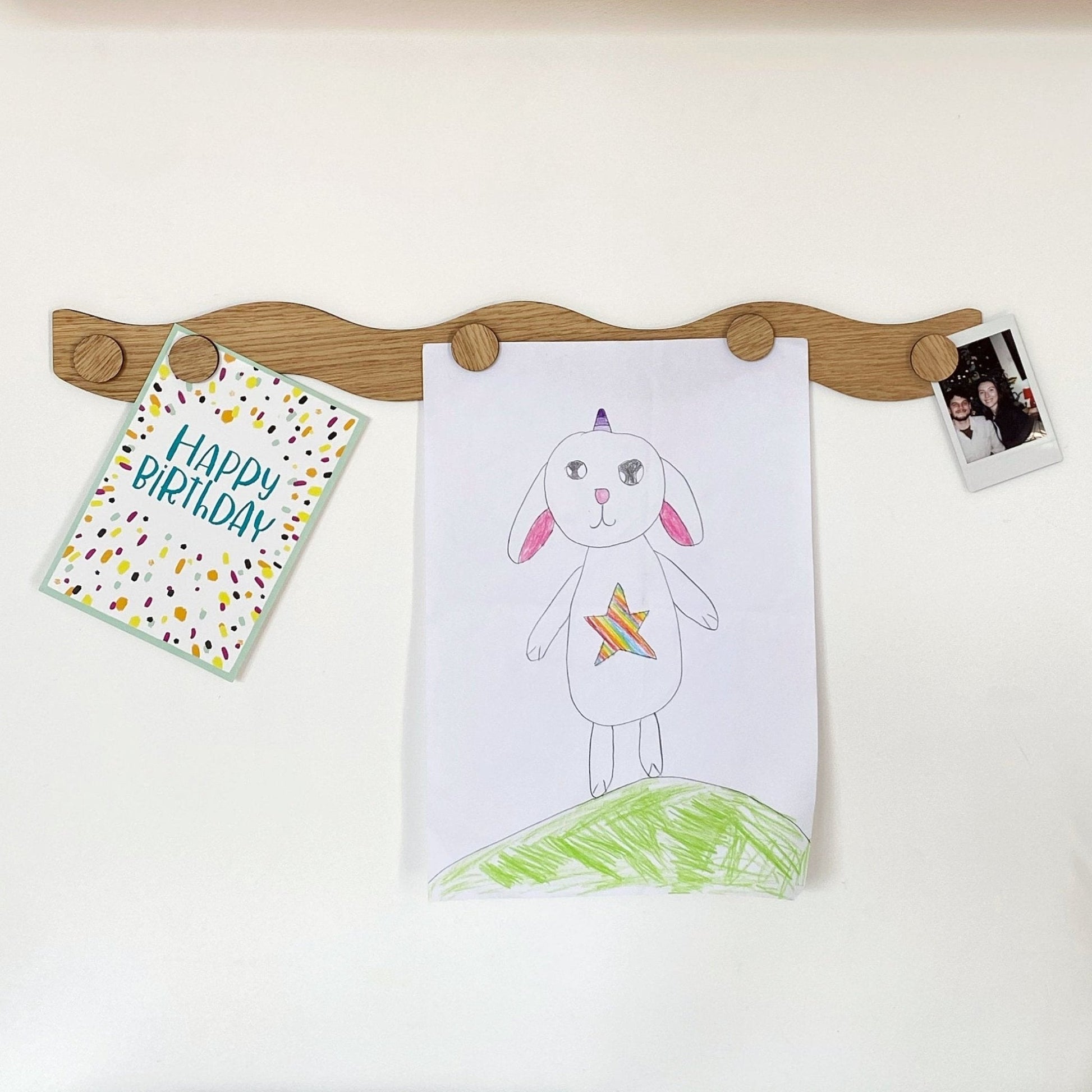 Wooden peg board with children's artwork and a card on a white background