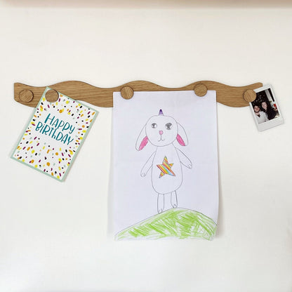 Wooden peg board with children's artwork and a card on a white background