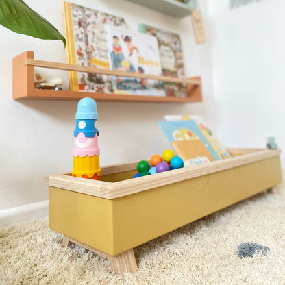 Children's play area with a yellow toy box, colorful toys, and shelves with books and decor.