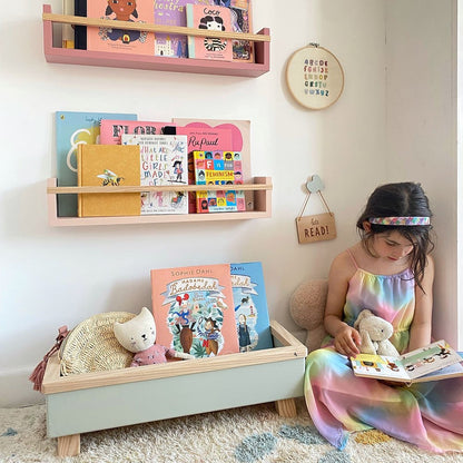 Child reading a book on the floor with colorful shelves displaying books in the background.