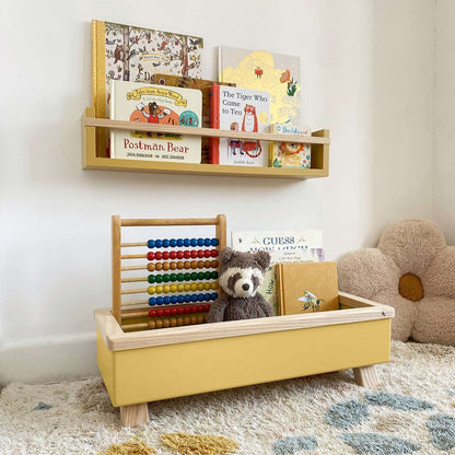 Yellow toy box with teddy bear, books, and abacus on a carpeted floor.