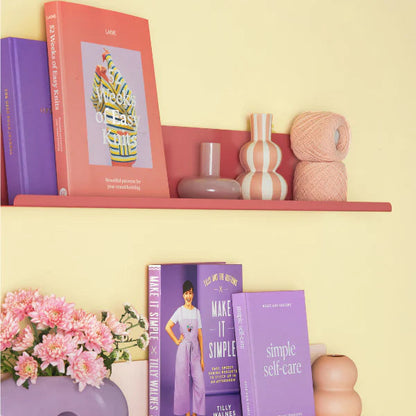 Shelves with books, decorative items, and flowers against a yellow wall