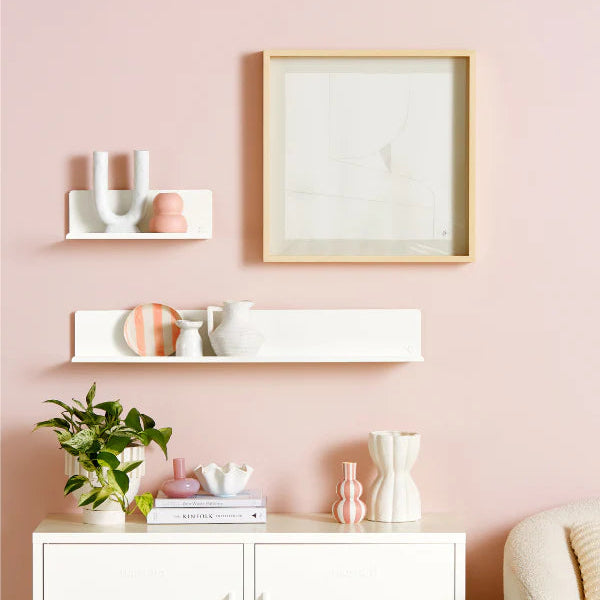 Decorative wall setup with a framed picture, shelves, and a cabinet against a pink wall.