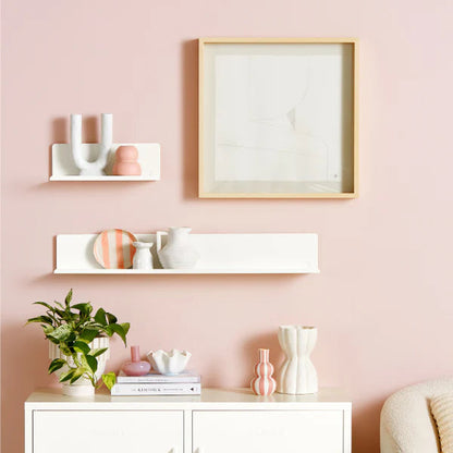 Decorative wall setup with a framed picture, shelves, and a cabinet against a pink wall.