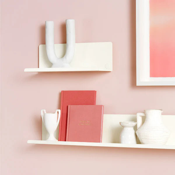 Pink office desk setup with shelves, books, and decor against a pink wall.