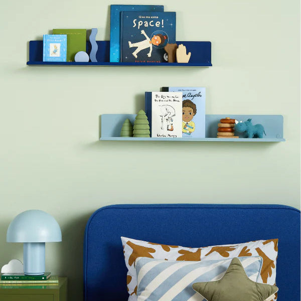 Children's bedroom with blue shelves, books, and a bed with colorful pillows.