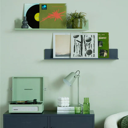 Vinyl records and a record player on a shelf against a light green wall.