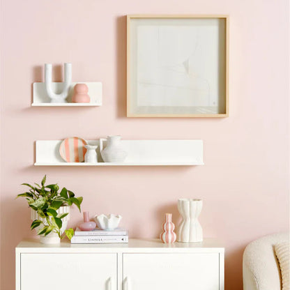 White cabinet with decorative items including a plant, basket, and bottles on a pink background