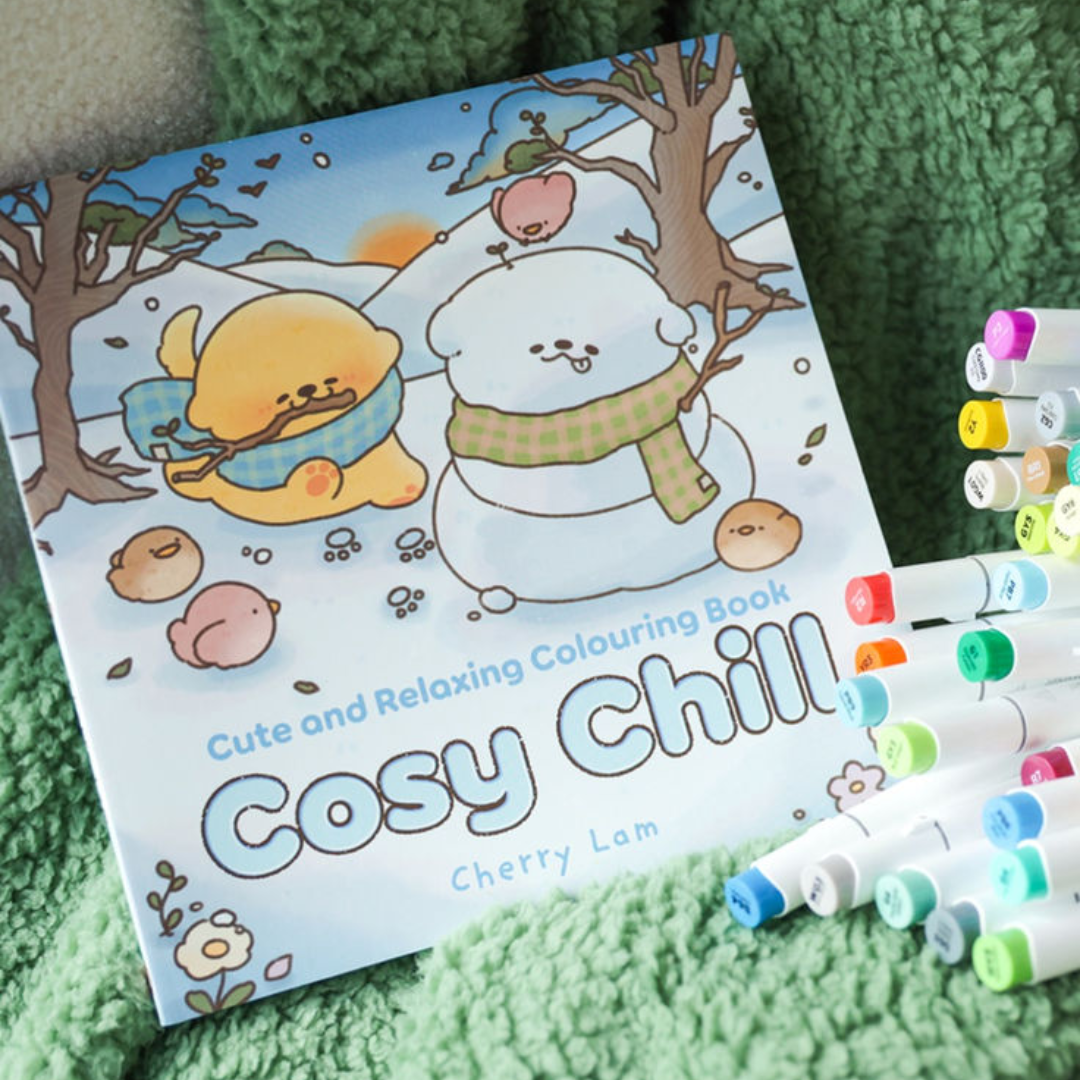 Coloring book titled 'Cosy Chill' with markers on a green surface