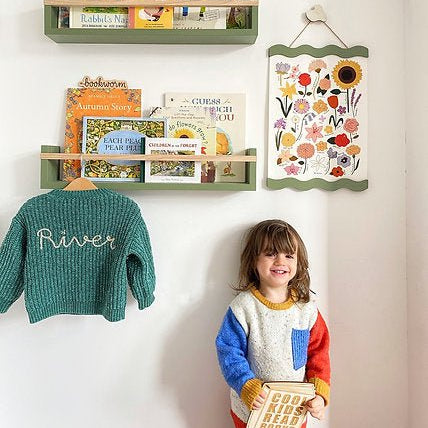 Children's room with bookshelves, books, and a child standing next to a wall decoration.