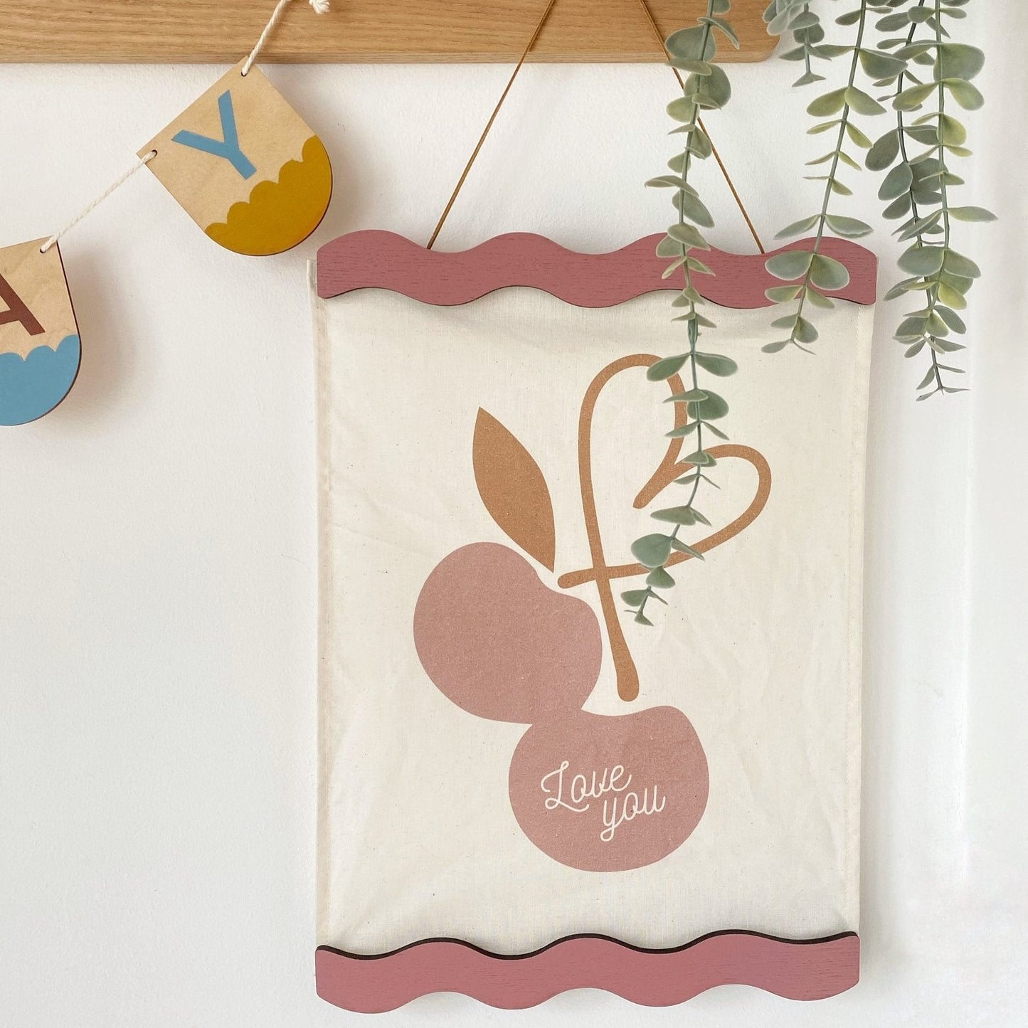 Decorative wall hanging with cherries and 'love you' text on a white wall.